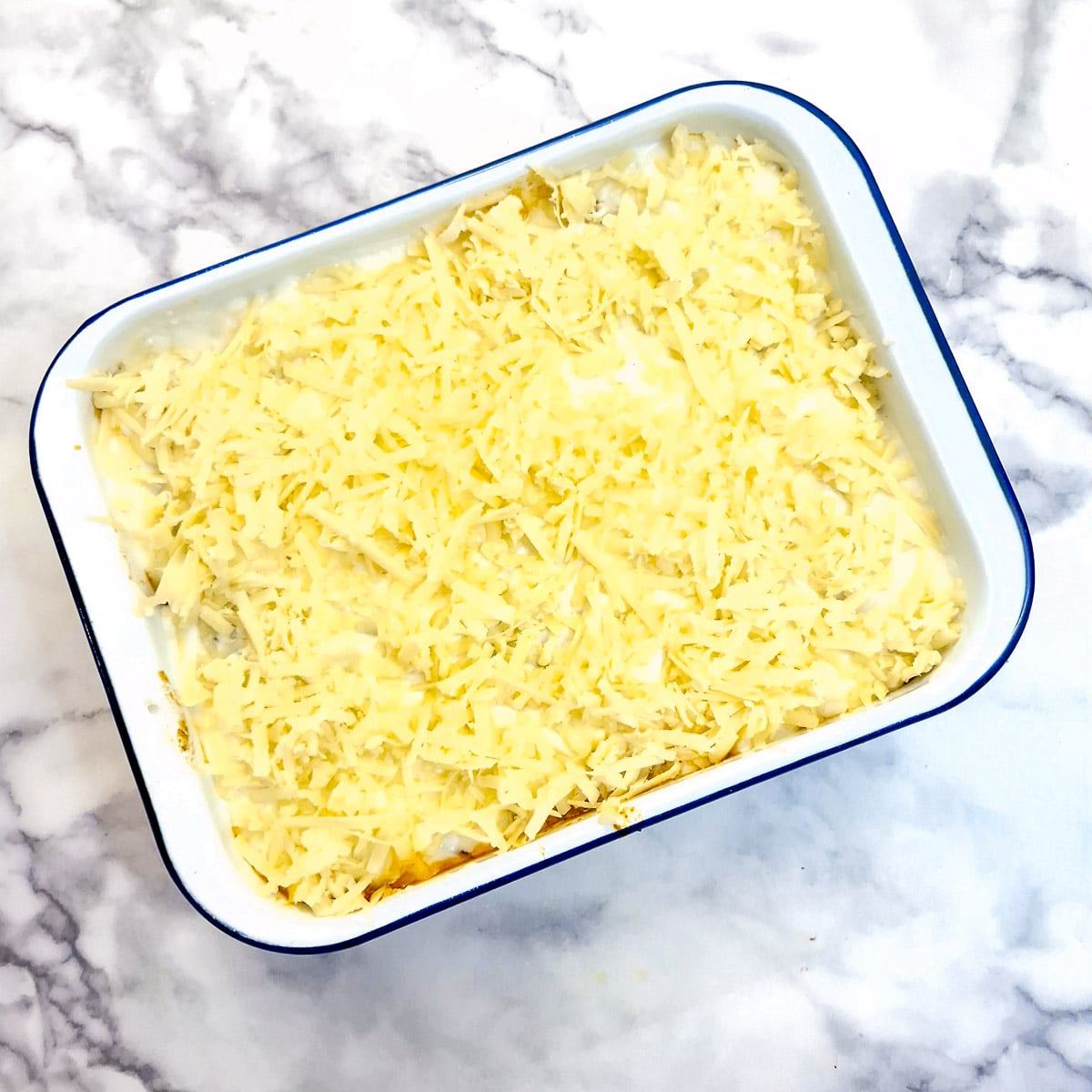 A fully assembled lasagne in a baking dish covered with grated cheese.