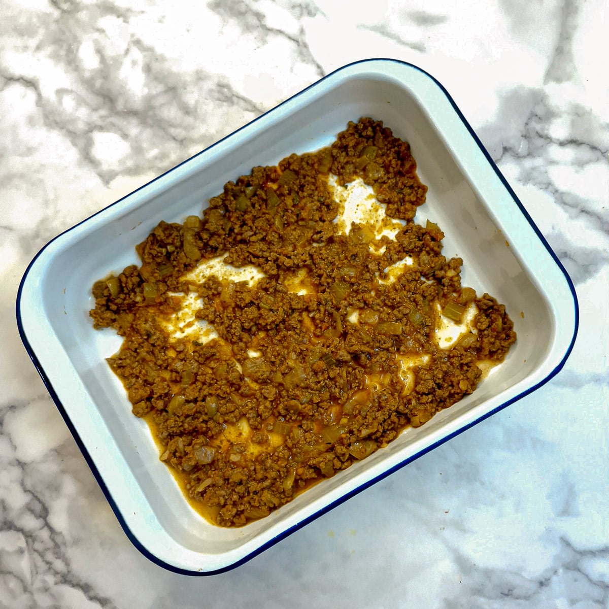 A layer of meat sauce in a baking dish.