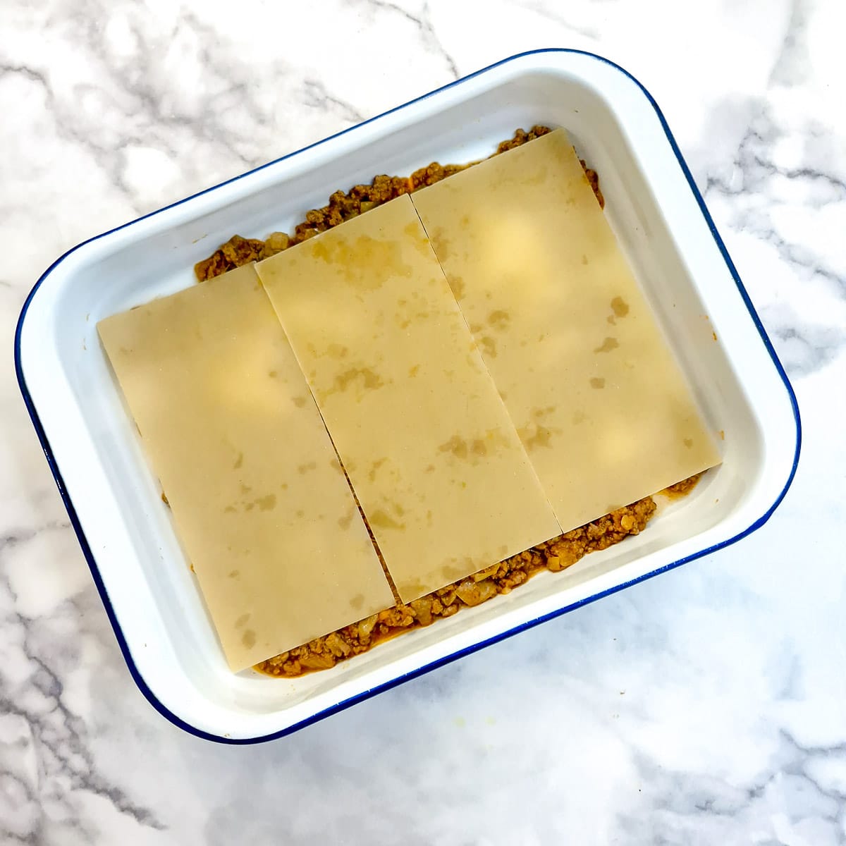 Three lasagne sheets on a layer of meat sauce.