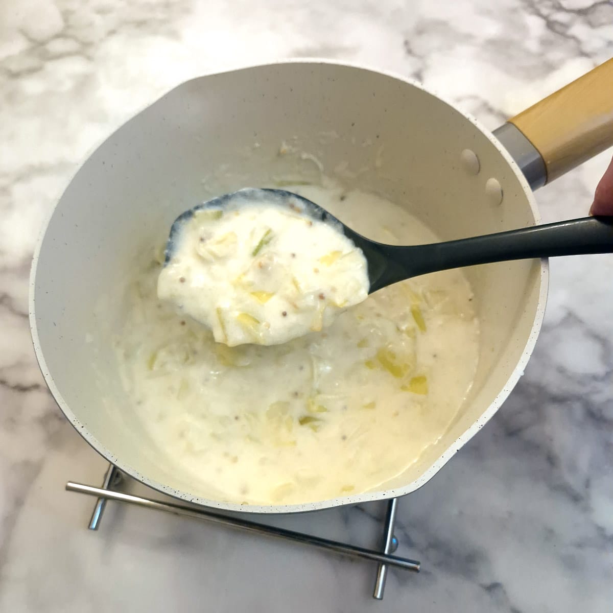 Leek and bechamel sauce held above the saucepan on a large spoon.