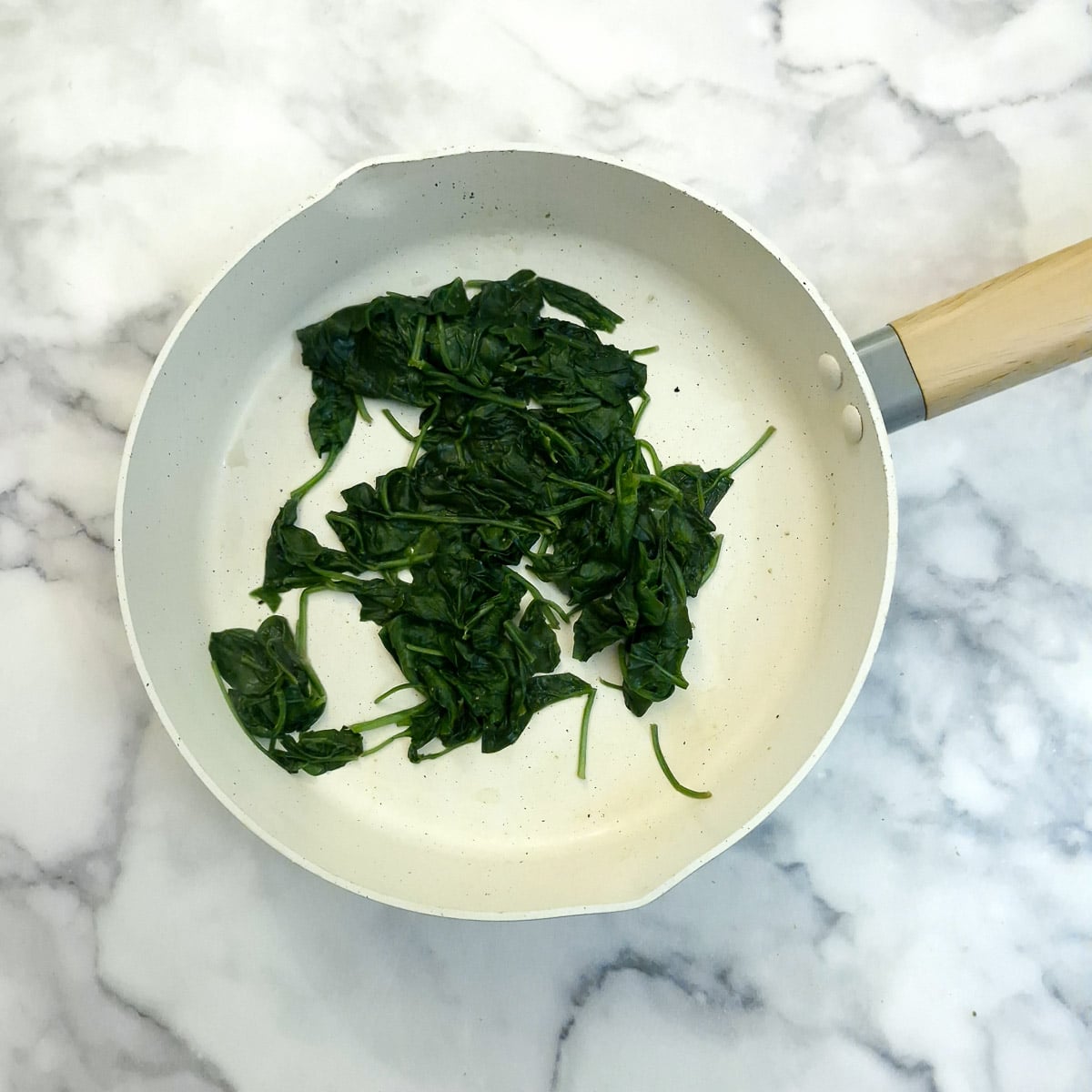 Wilted baby spinach leaves in a saucepan.
