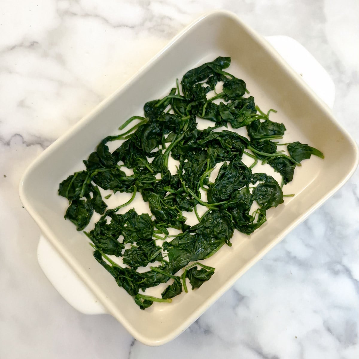 Wilted baby spinach leaves arranged on the bottom of a casserole dish.