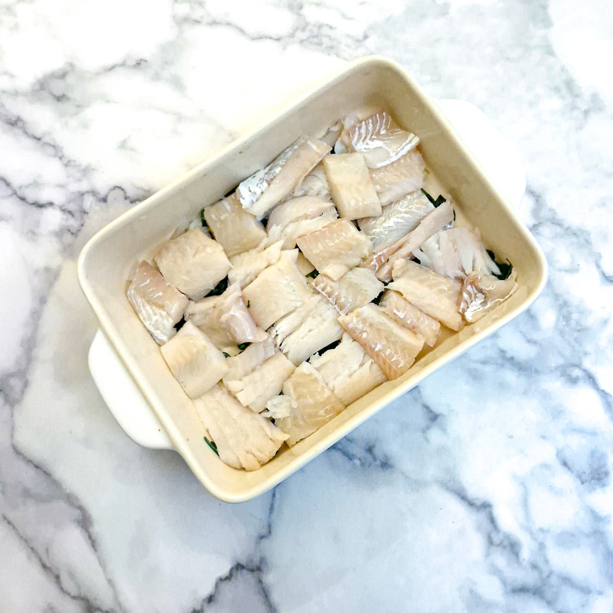 Bite-sized pieces of haddock arranged on top of spinach in a casserole dish.