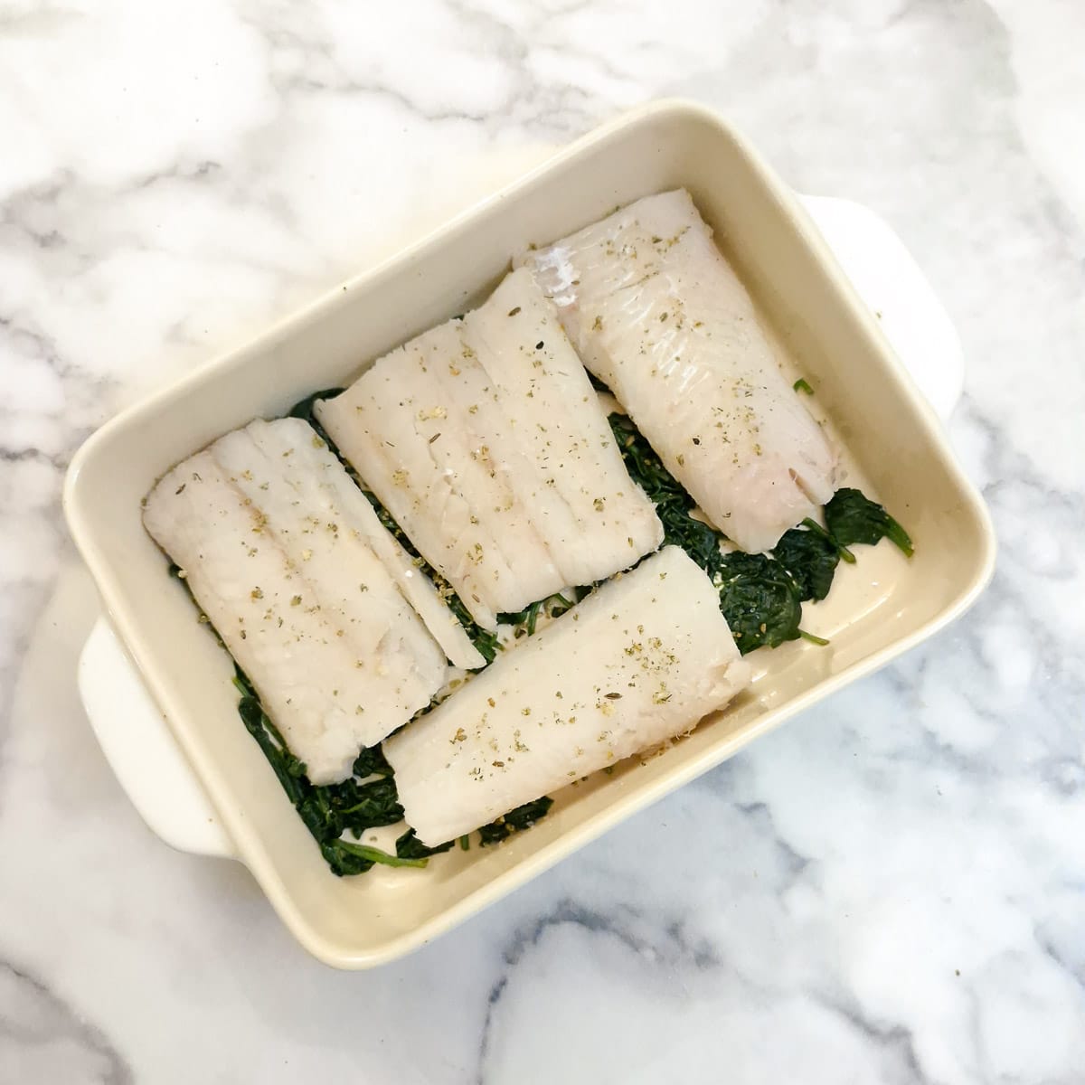 Whole fillets of haddock arranged on top of spinach in a casserole dish.