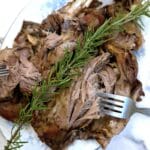 A slow roasted lamb shoulder being shredded with two forks.