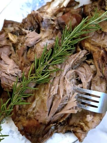 A slow roasted lamb shoulder being shredded with two forks.