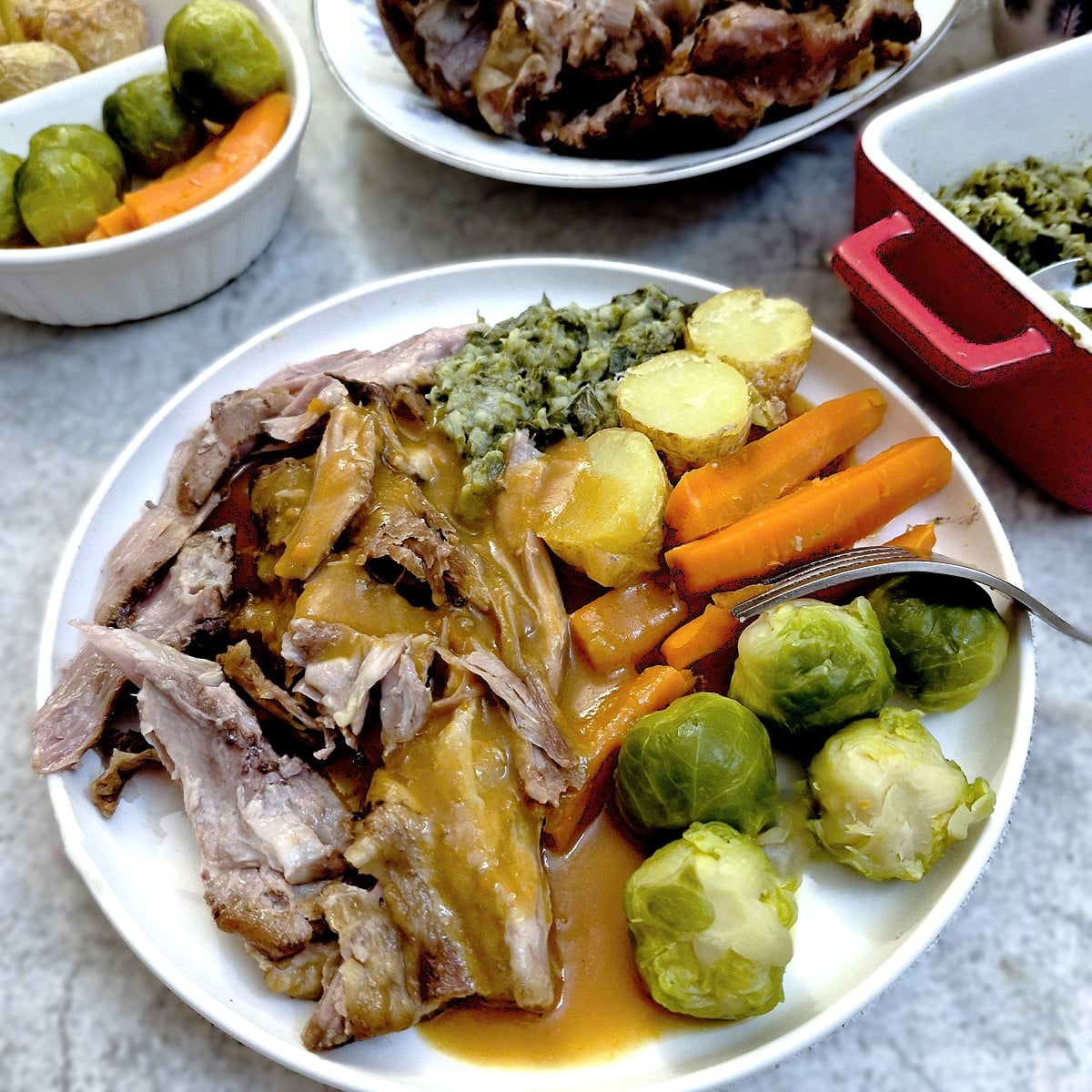 A white place of slow-roasted lamb shoulder with vegetables and gravy.