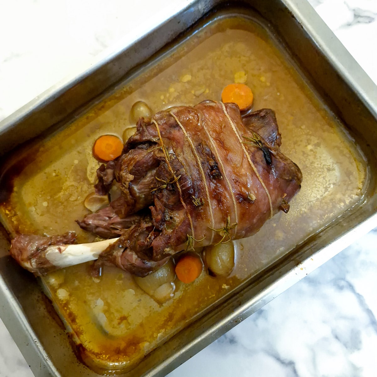 A fully cooked lamb shoulder in a roasting pan.