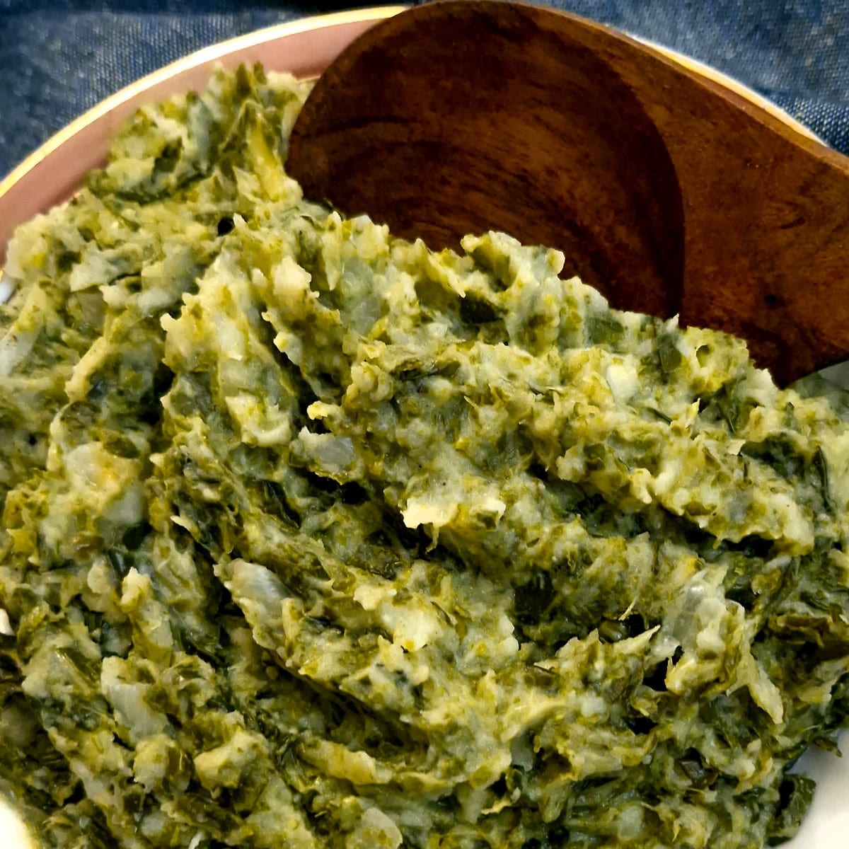 Close up of mashed spring greens and potatoes with a large wooden serving spoon.