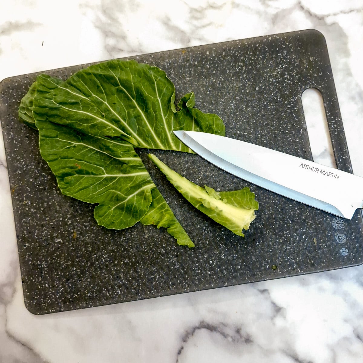 A leaf of spring greens on a chopping board with the centre stalk removed.