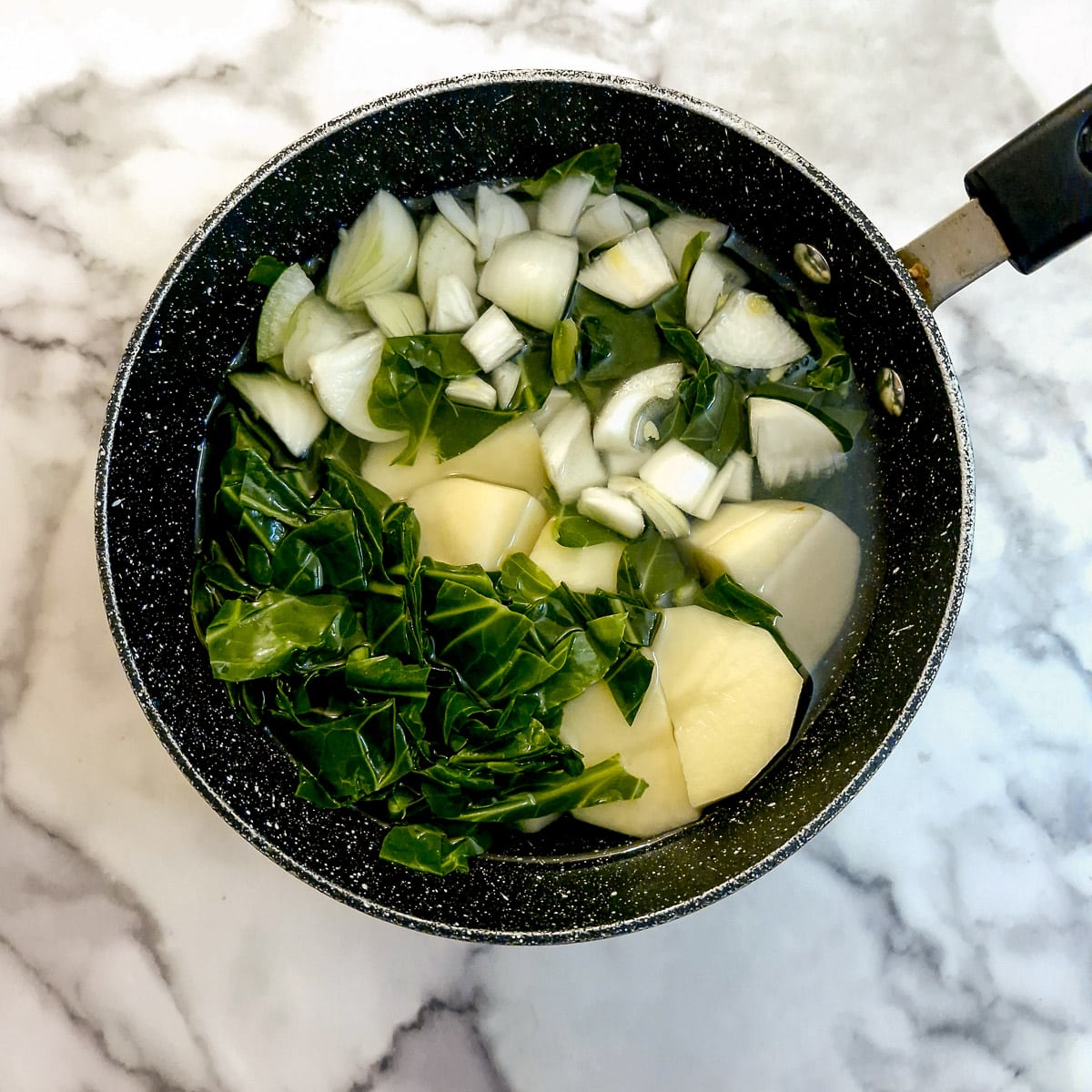 Blanched spring greens with potatoes and onions in a saucepan.