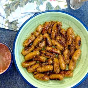 A green serving dish of sticky honey mustard glazed cocktail sausages.