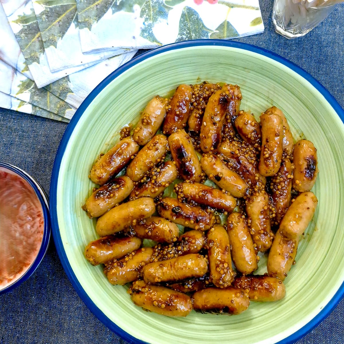 A green serving dish of sticky honey mustard glazed cocktail sausages.
