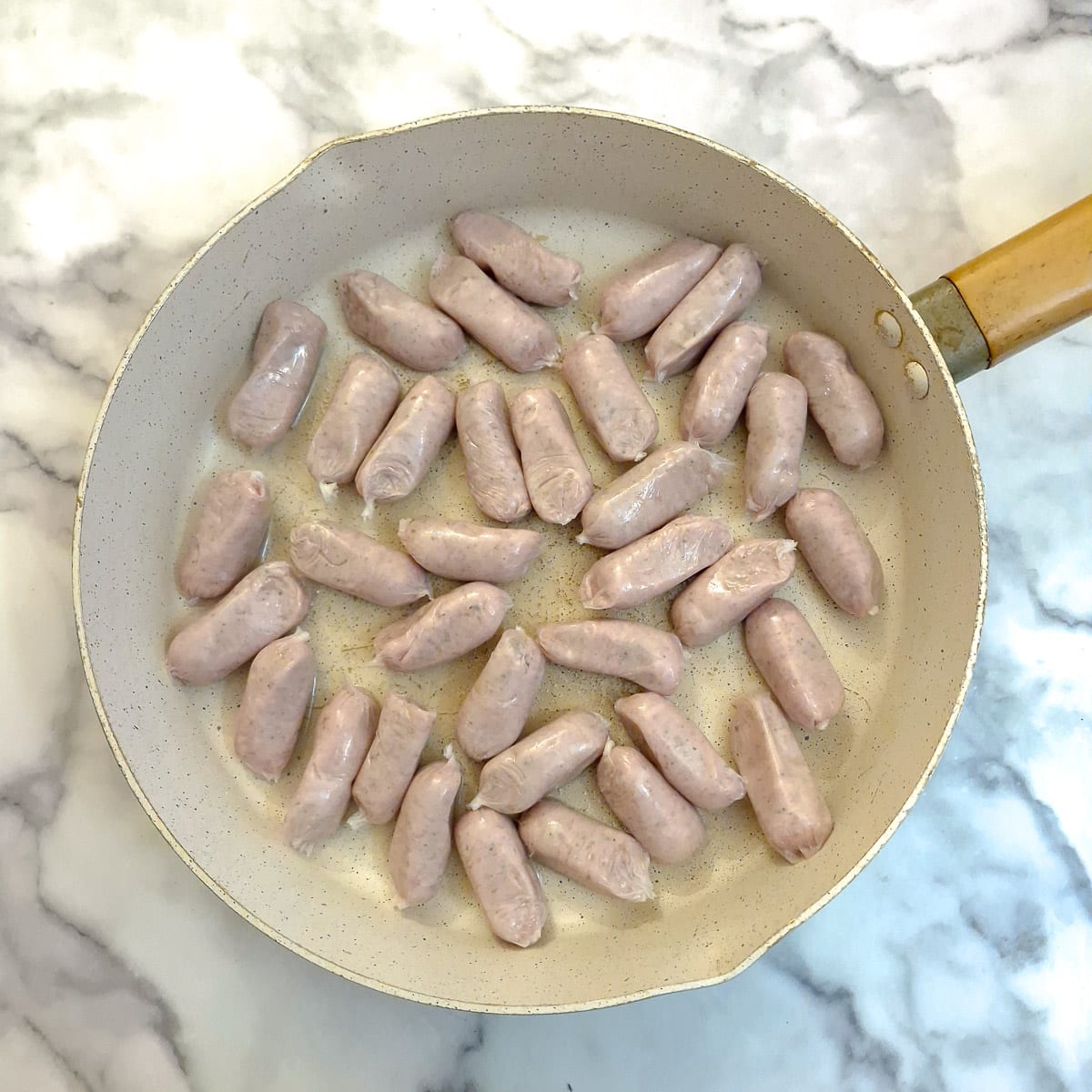 Uncooked cocktail sausages in a frying pan.