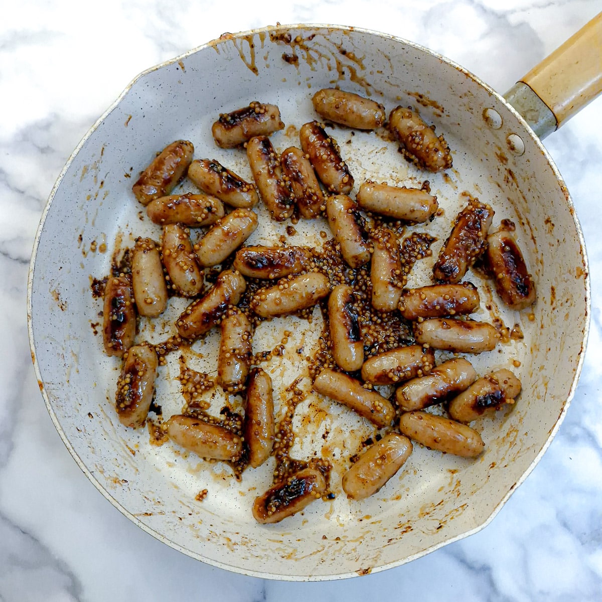 Cooked sausages in a frying pan with honey and whole-grain mustard.