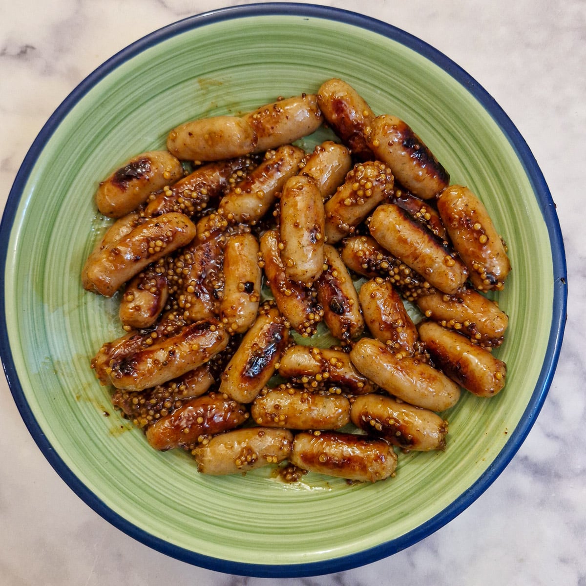 Oerhead shot of glazed cocktail sausages in a green serving dish.