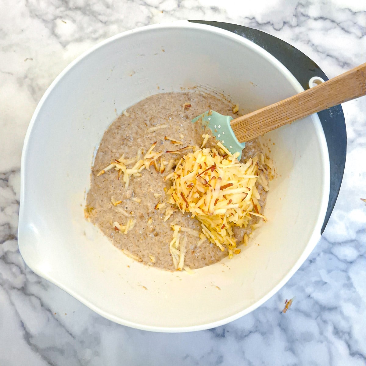 Grated apples added to the bowl of muffin batter.