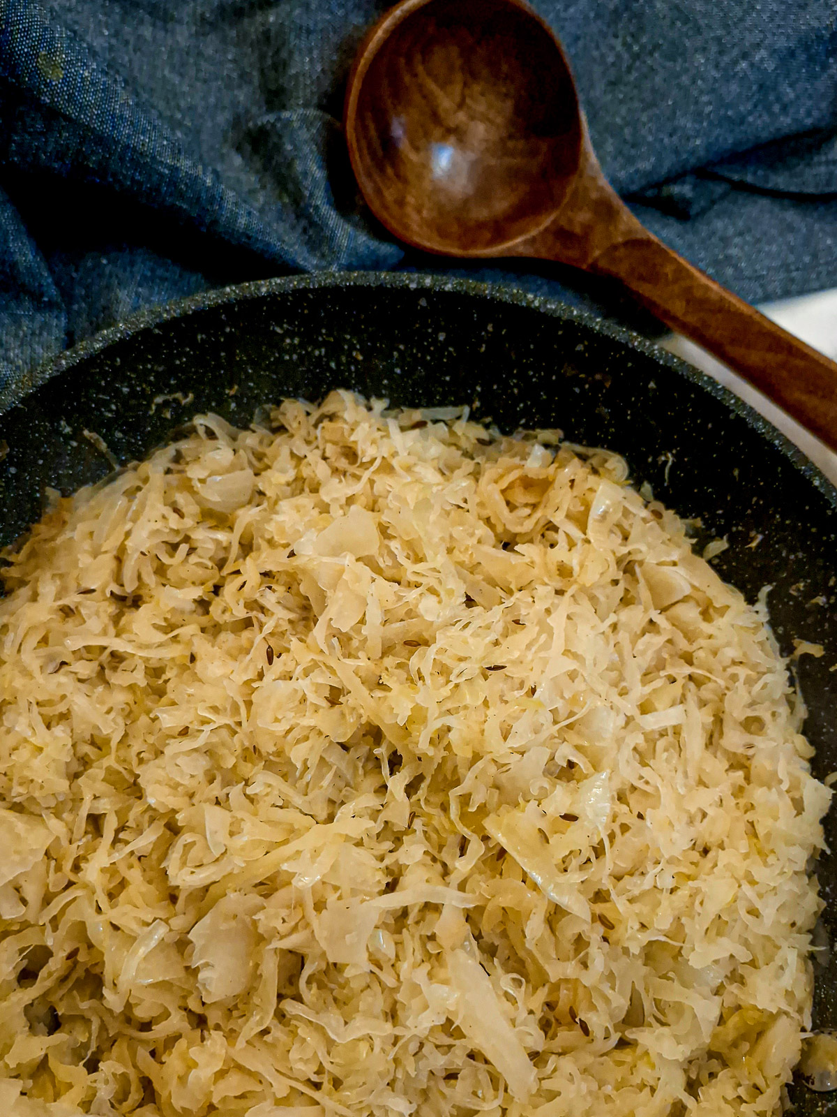 Close up of a dish of sauerkraut next to a large wooden spoon.
