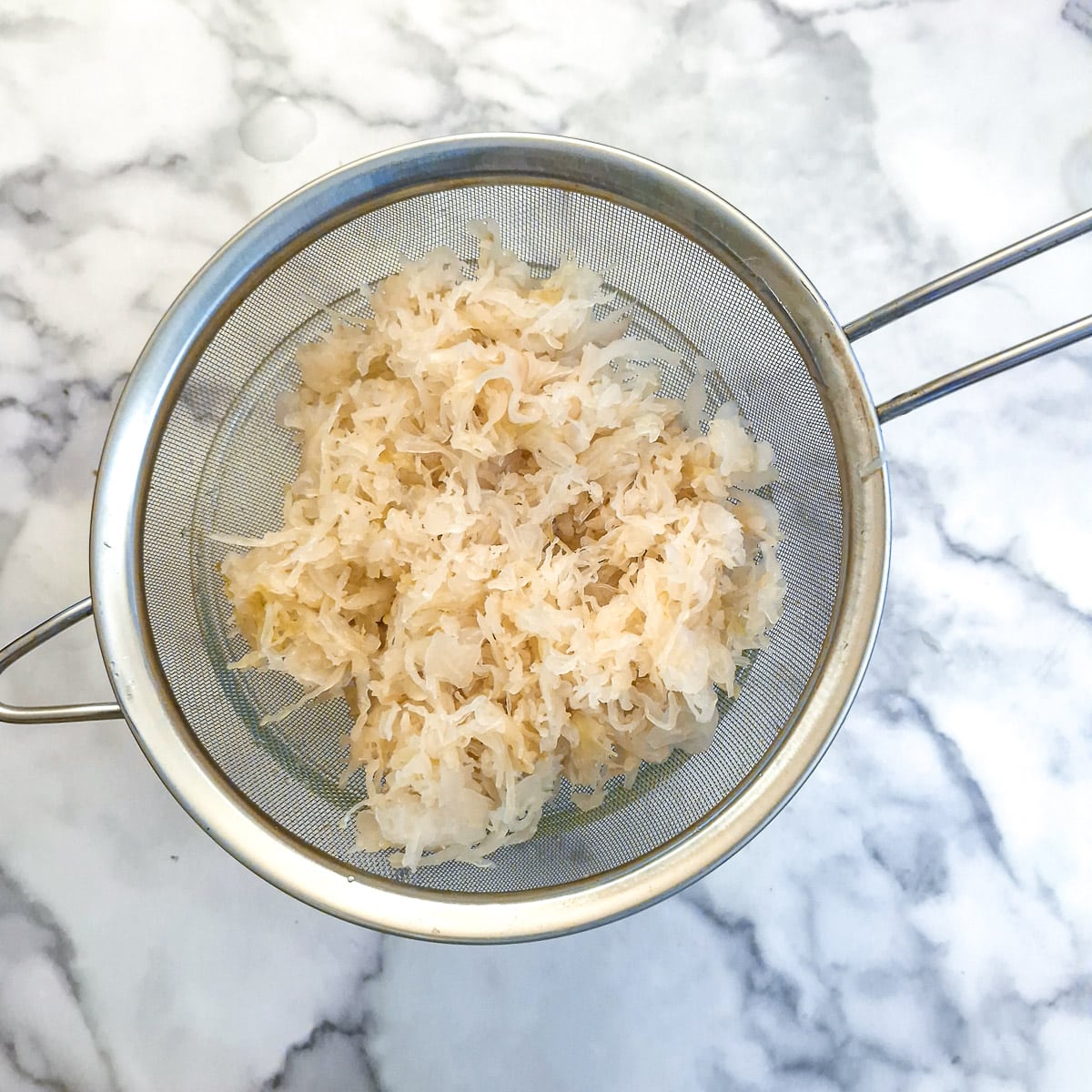 Sauerkraut draining in a sieve over a glass bowl.
