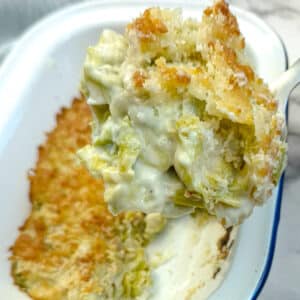 A spoonful of leek and brussels sprouts bake being lifted from a casserole dish with a large spoon.