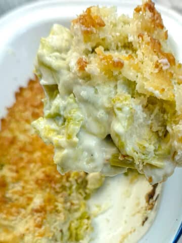 A spoonful of leek and brussels sprouts bake being lifted from a casserole dish with a large spoon.
