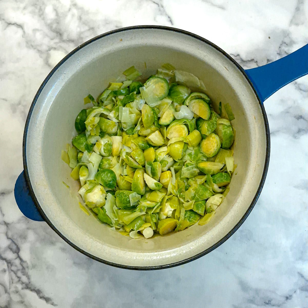 Softened leeks and brussels sprouts in a saucepan.