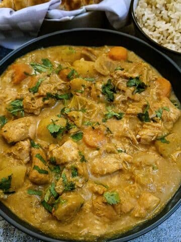 A dish of slow cooker chicken curry next to a small bowl of brown rice.