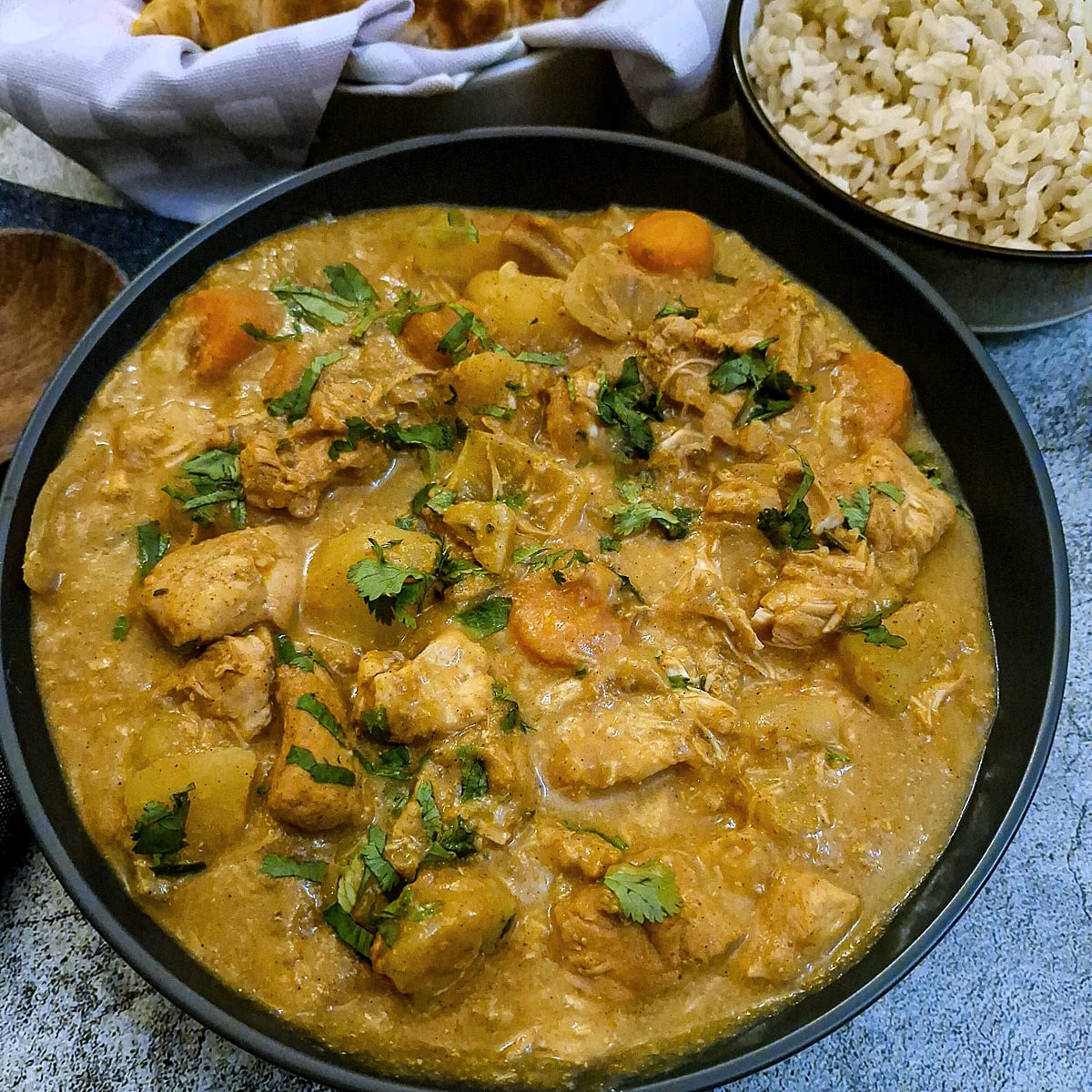 A dish of slow cooker chicken curry next to a small bowl of brown rice.