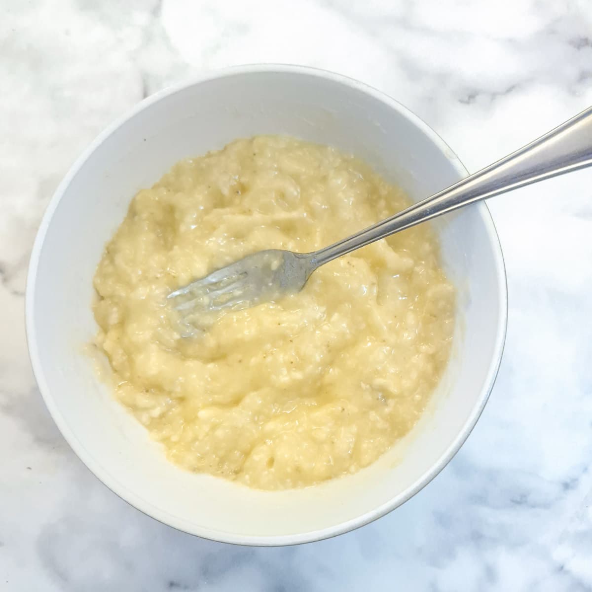 Mashed banana in a small bowl with a fork.