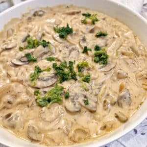 Close up of hunter's sauce garnished with parsley in a white serving dish.