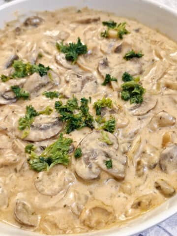 Close up of hunter's sauce garnished with parsley in a white serving dish.
