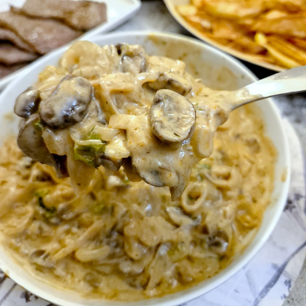 A spoonful of mushroom sauce being lifted from a serving dish.