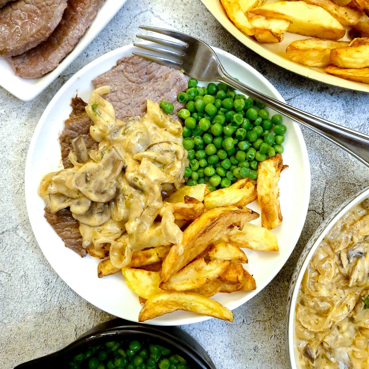 A plate of steak, chips and peas smothered in hunter's sauce.