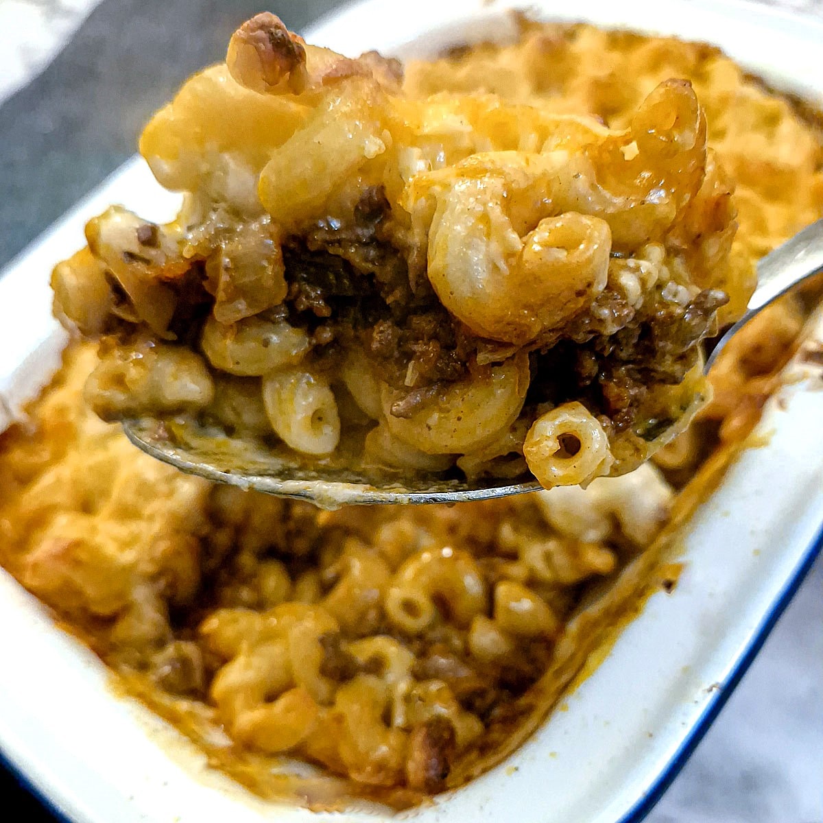 Closeup of a spoonful of macaroni and cheese lasagne being lifted from the baking dish.