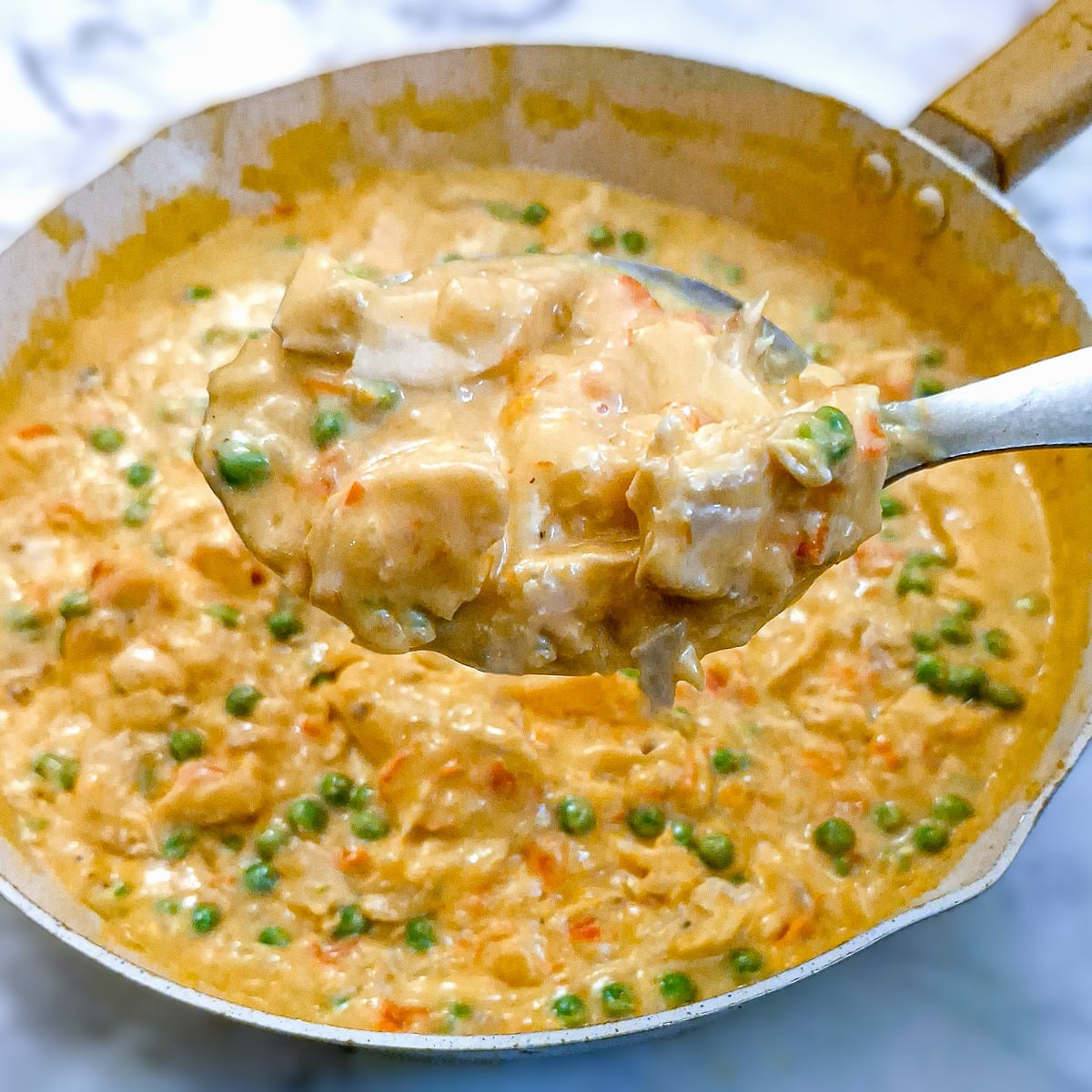 Close up of poached salmon in red pepper sauce on a large spoon held over the pan.