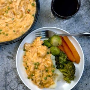 Poached salmon in creamy red pepper sauce on a white plate with vegetables.