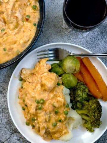 Poached salmon in creamy red pepper sauce on a white plate with vegetables.