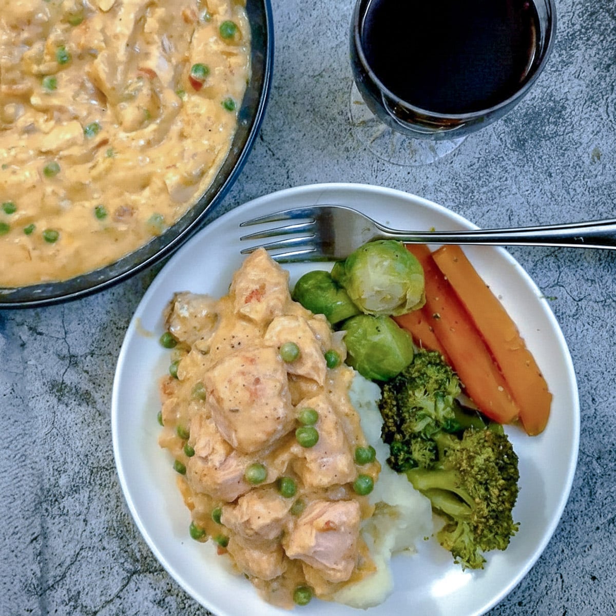 Poached salmon in creamy red pepper sauce on a white plate with vegetables.