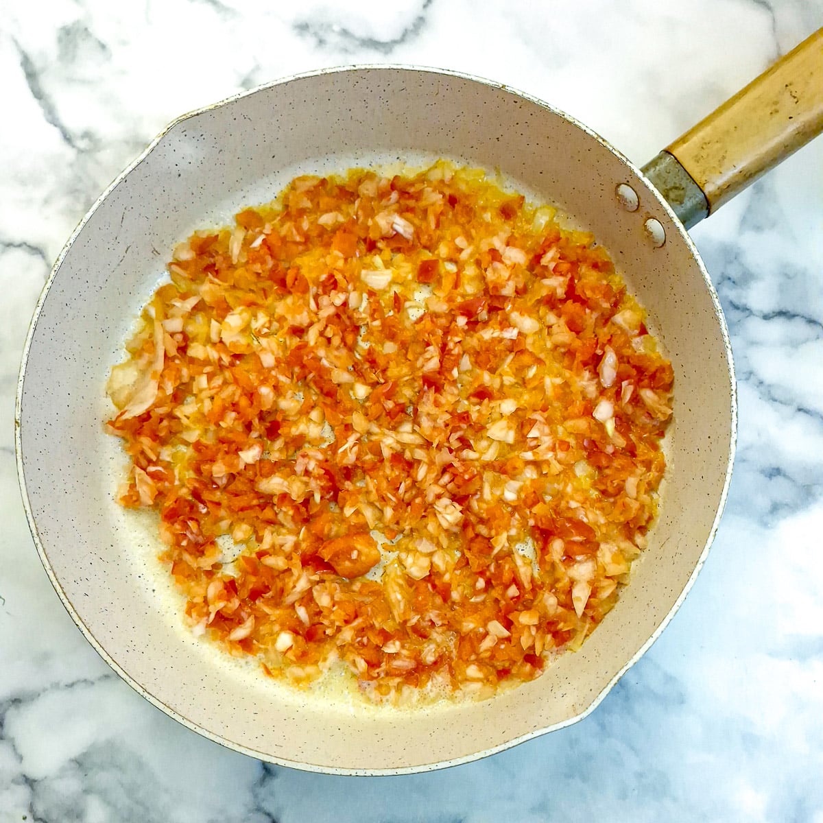 Finely chopped onion and red pepper cooking in a frying pan.