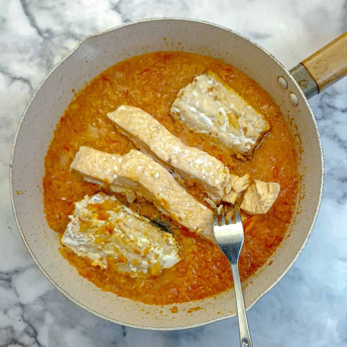 Poached salmon fillets nestled in a bed of red pepper sauce in a frying pan.