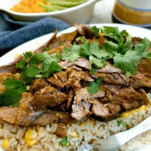 Close up of slices of curried slow cooked lamb on a bed of rice and peas.