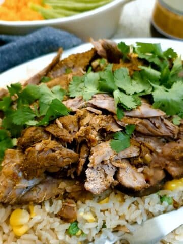 Close up of slices of curried slow cooked lamb on a bed of rice and peas.