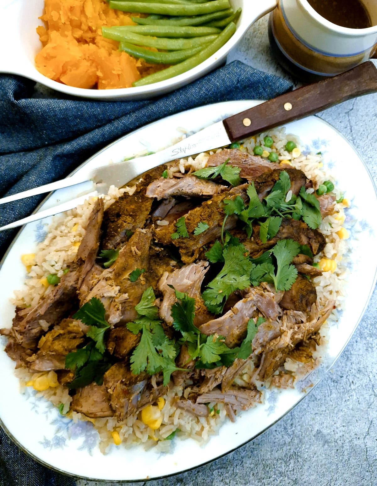Overhead shot of a serving plate with sliced lamb on a bed of rice garnished with fresh coriander leaves.