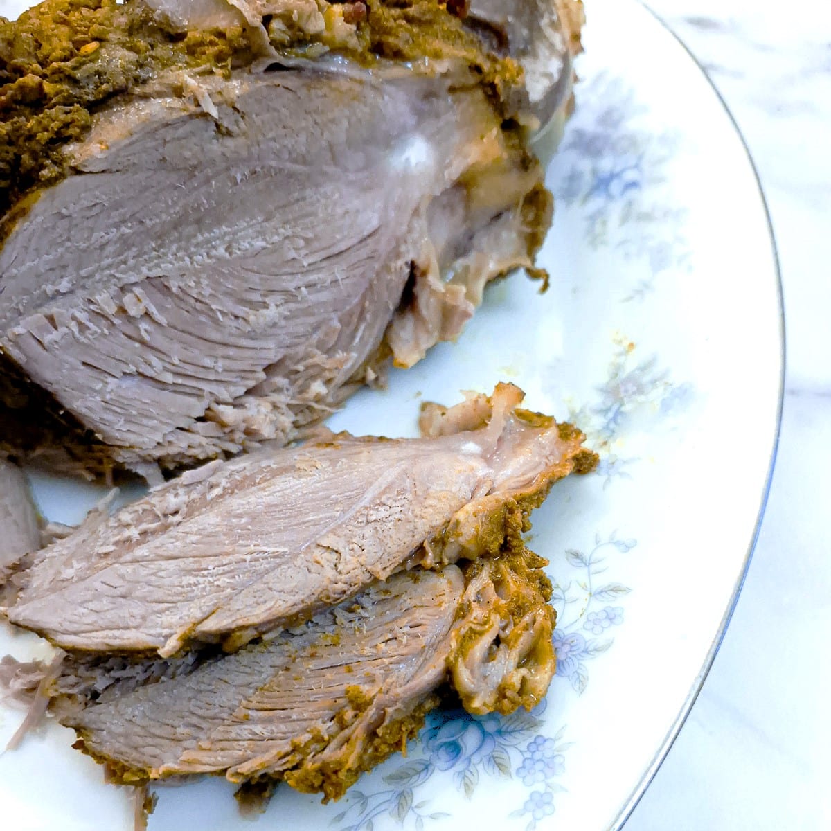 Slices of slow-cooked curried leg of lamb on a serving plate.