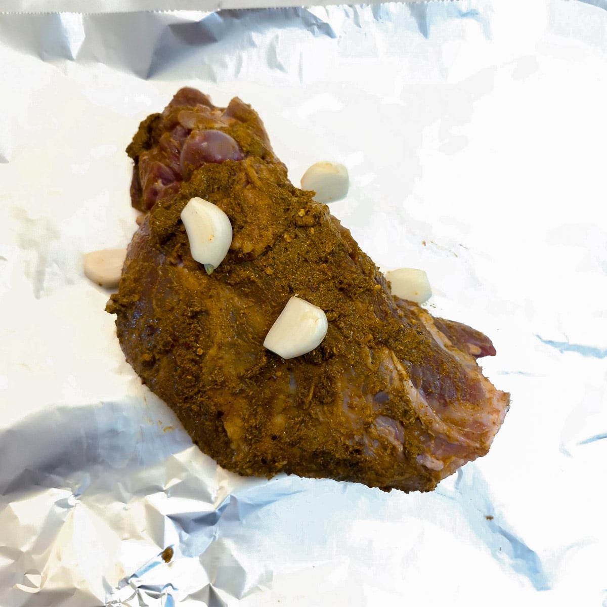 Curry coated leg of lam on a sheet of tin foil with cloves of garlic.