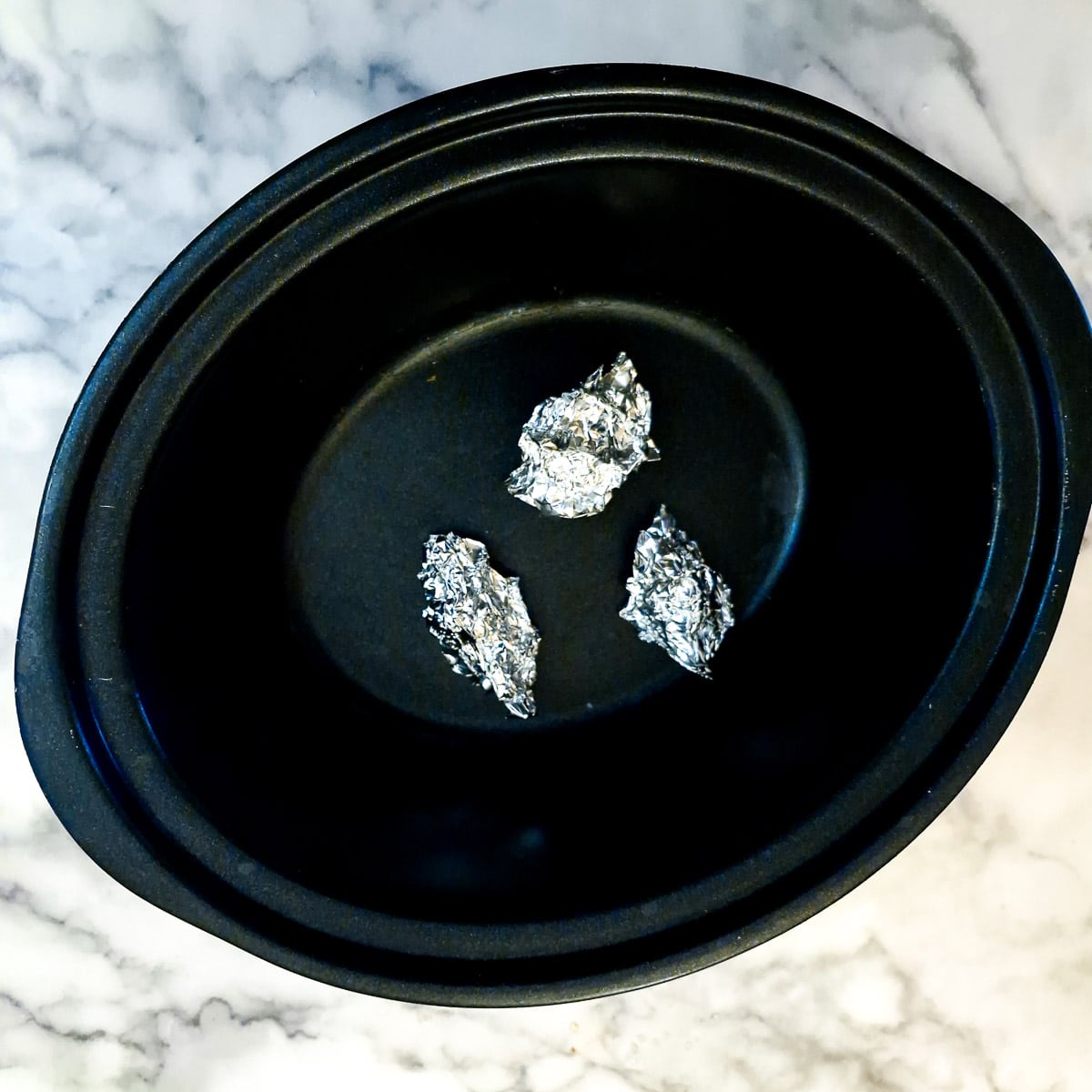 Three small balls of tin foil on the base of a slow cooker.