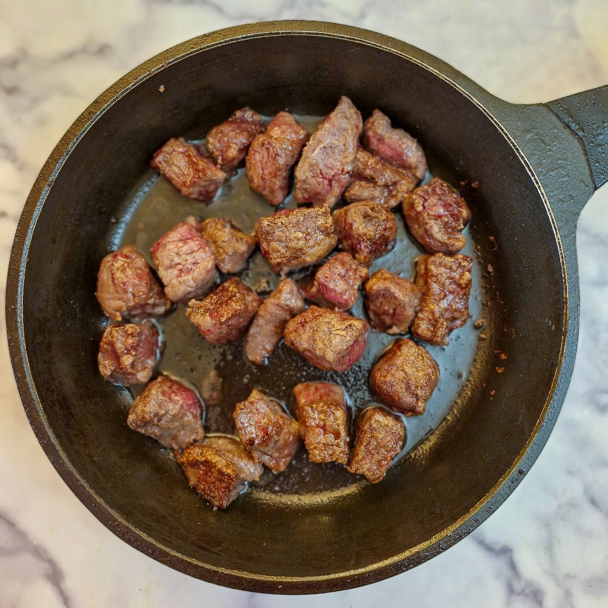 Beef cubes browniing in a frying pan.