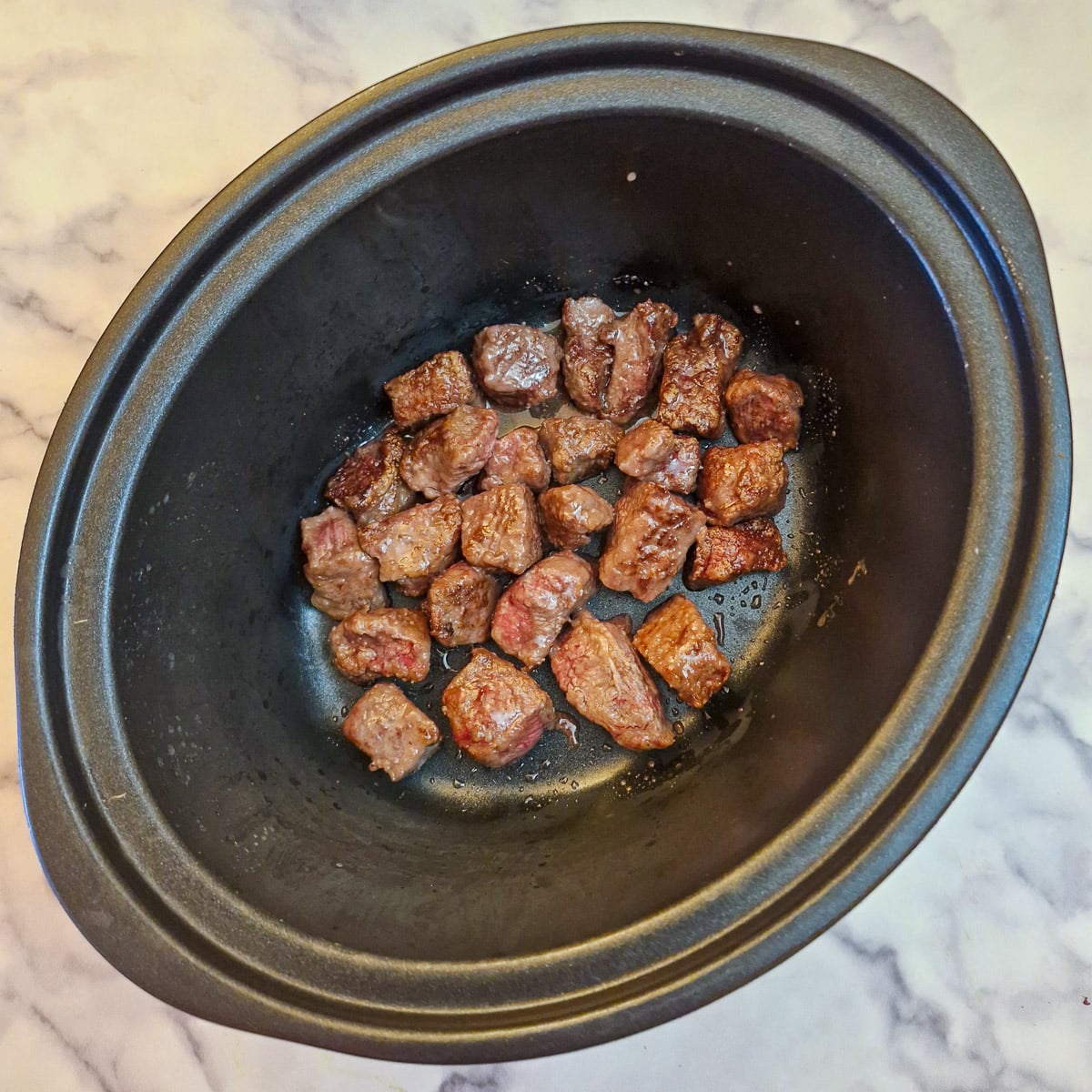 Browned beef cubes in a slow cooker.
