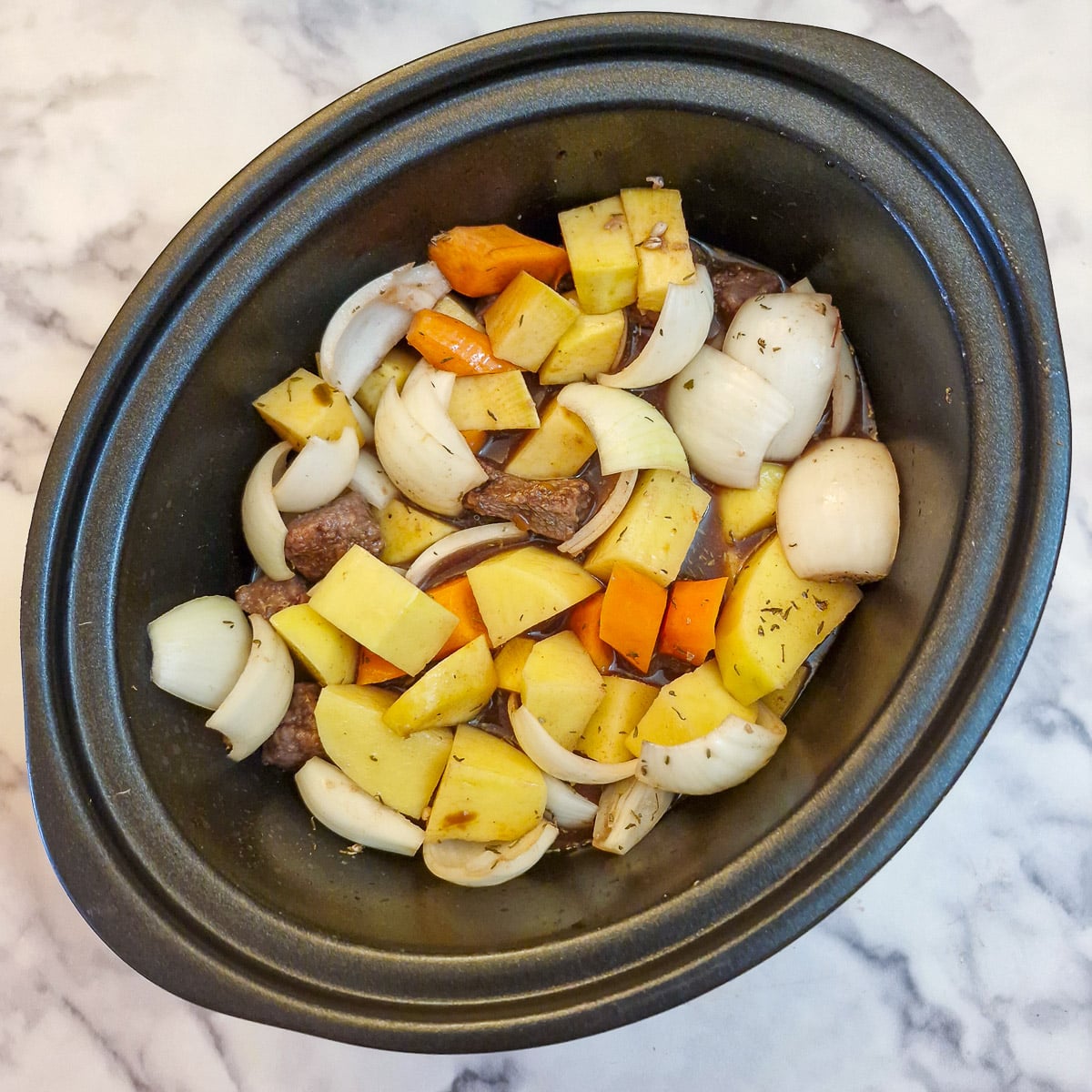 Stock and red wine poured over the vegetables and beef in a slow cooker.