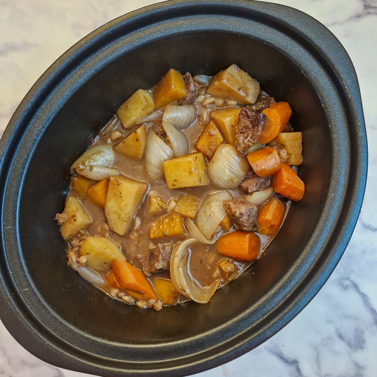 Cooked beef and vegetables with gravy in a slow cooker.